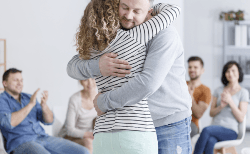 Picture of a couple hugging during group therapy, chair and people arranged in a circle