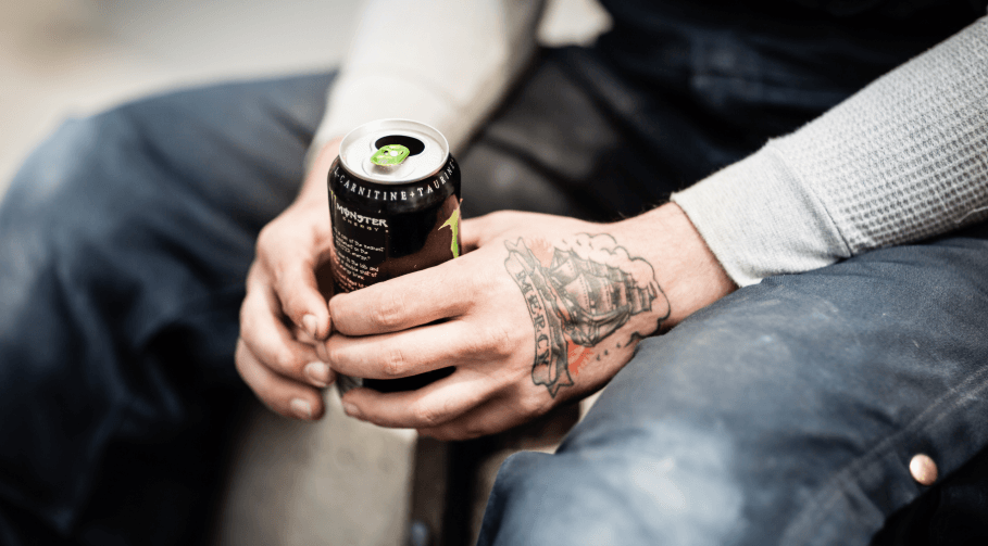 A person holding a can with a tattoo on their hand